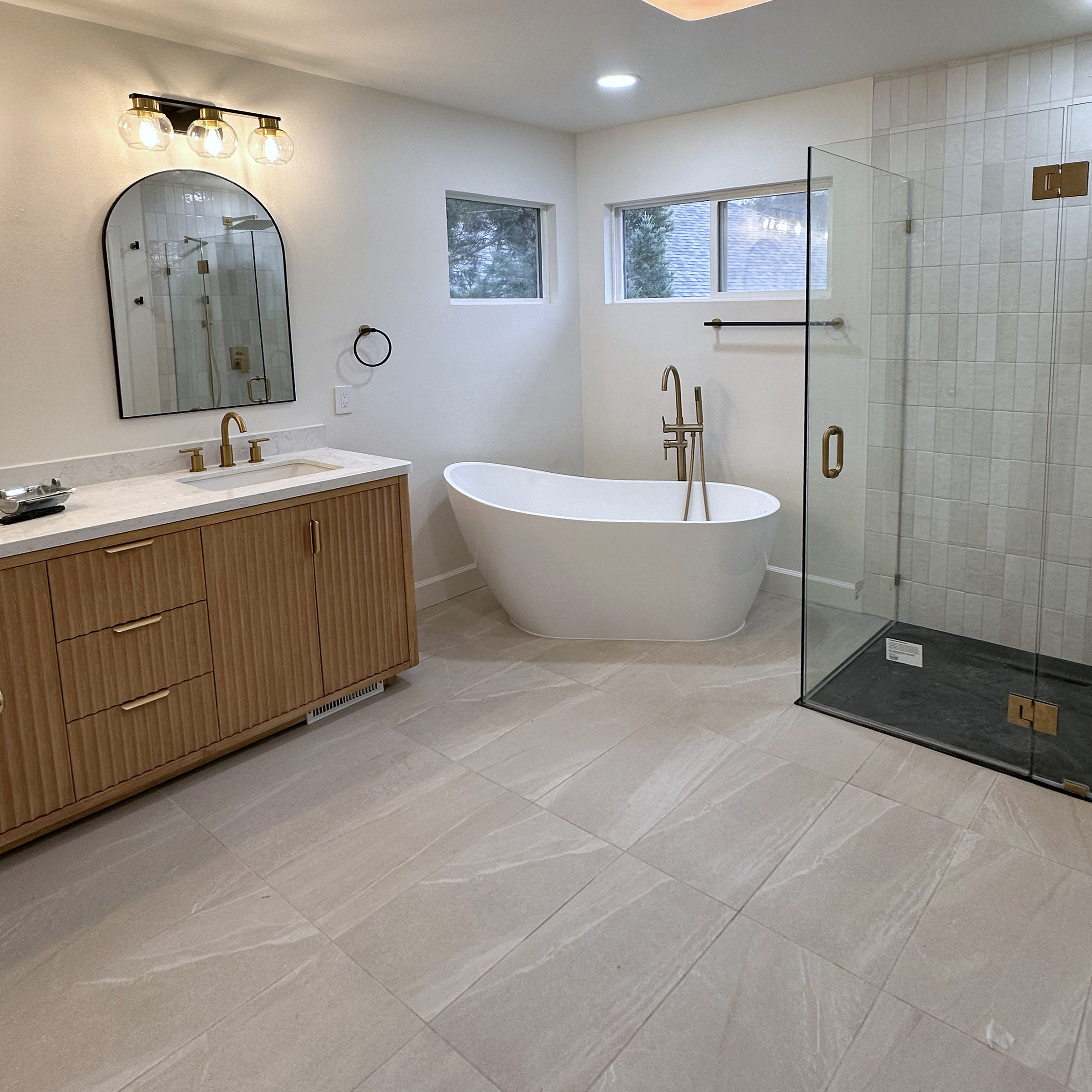 Bathroom with a fluted wood vanity, freestanding tub and glass shower.
