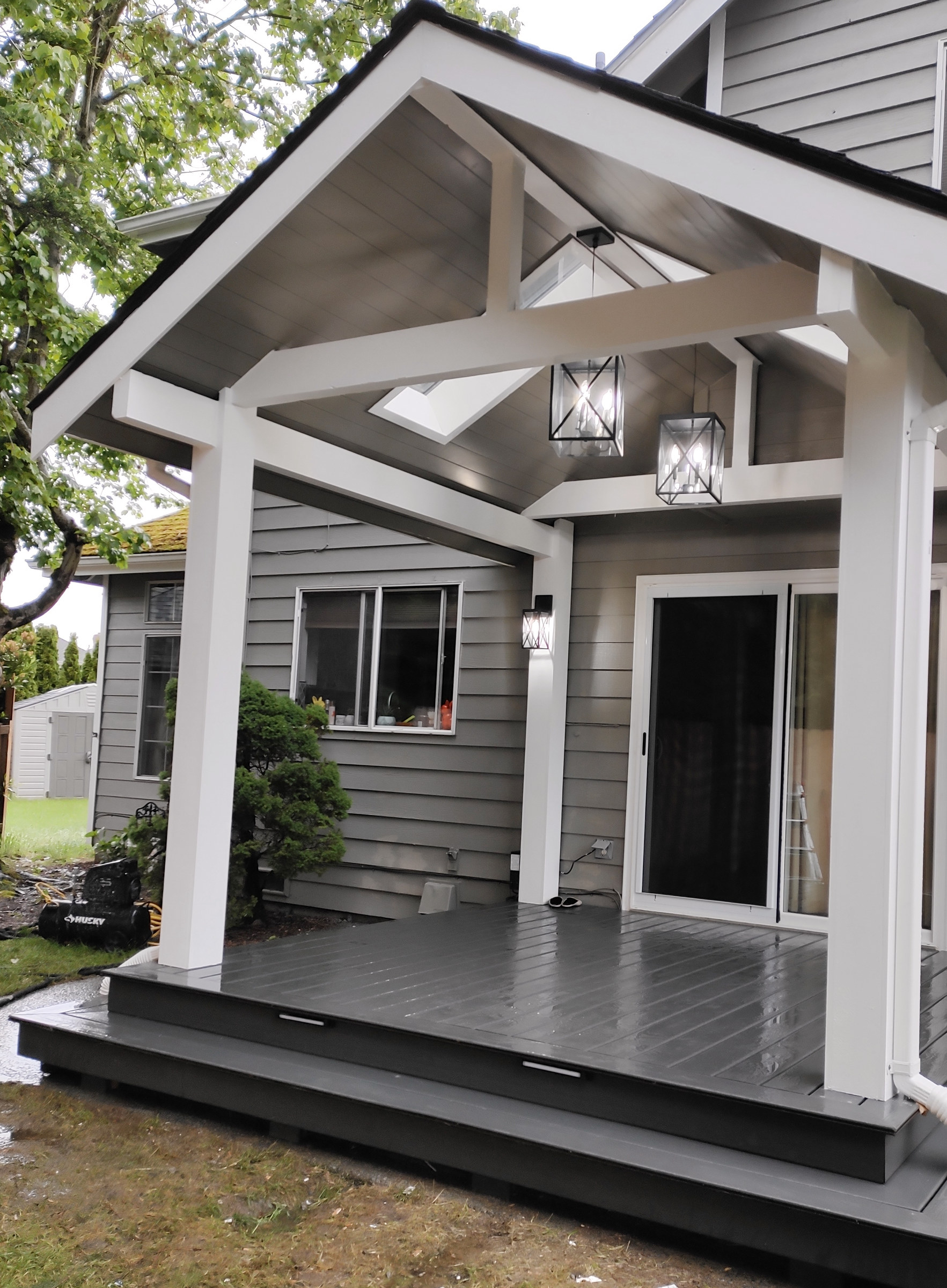 Covered porch with white beams, gray siding and glass pendant lanterns.