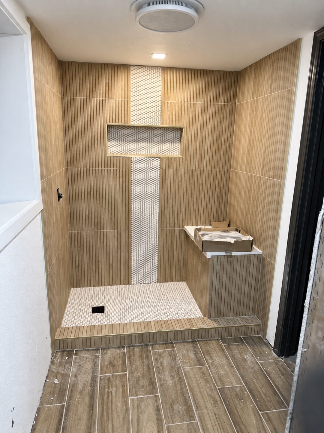 Wood-look shower tile and penny-tile niche during construction, before fixtures and final cleanup