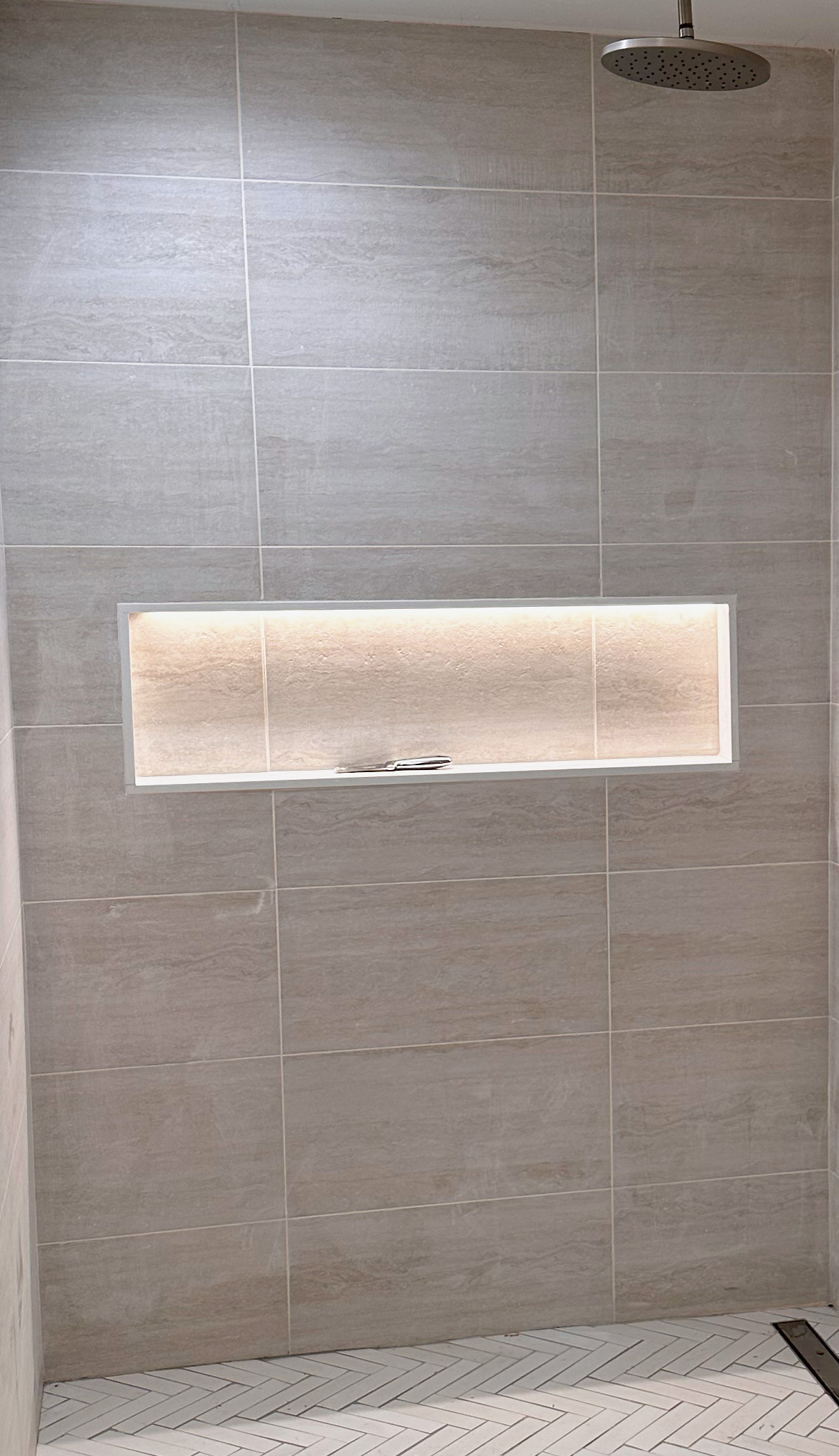Tiled shower with an illuminated niche and herringbone floor tile.